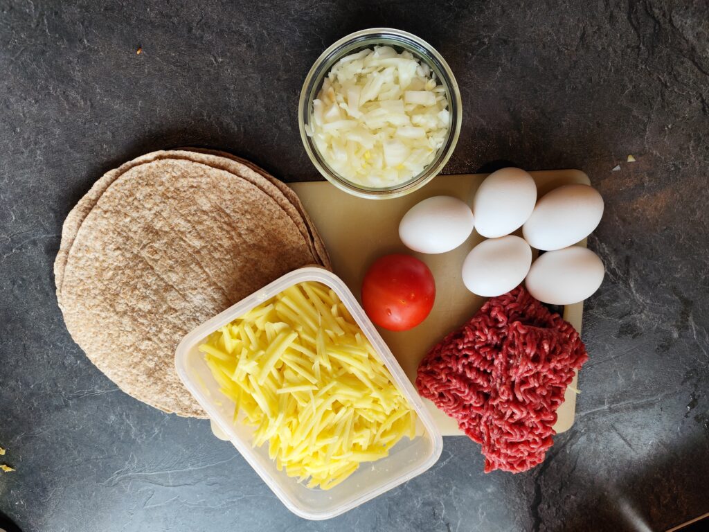 Ingredienser til morgenmadsburrito: hakket oksekød, æg, ost, løg, kartofler og tortilla til campingmad