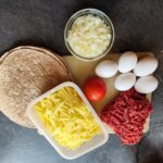 Ingredienser til morgenmadsburrito: hakket oksekød, æg, ost, løg, kartofler og tortilla til campingmad