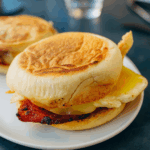 Hjemmebagte engelske breakfast muffins flækket og let ristede, klar til at blive fyldt med æg, bacon og ost.