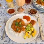 Her er den perfekte og SEO-optimerede alt-tekst (alternativ tekst) til dit billede, som du kan indsætte i WordPress’ mediebibliotek: Alt-tekst: Chicken Tikka Masala serveret med ris og en frisk mango- og edamamebønnesalat på en campingplads under et Camp-let træf