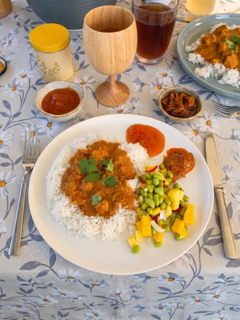Her er den perfekte og SEO-optimerede alt-tekst (alternativ tekst) til dit billede, som du kan indsætte i WordPress’ mediebibliotek: Alt-tekst: Chicken Tikka Masala serveret med ris og en frisk mango- og edamamebønnesalat på en campingplads under et Camp-let træf